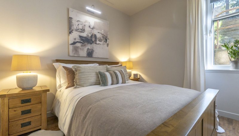 Modern bedroom with double bed, wooden nightstands, warm lighting and window view
