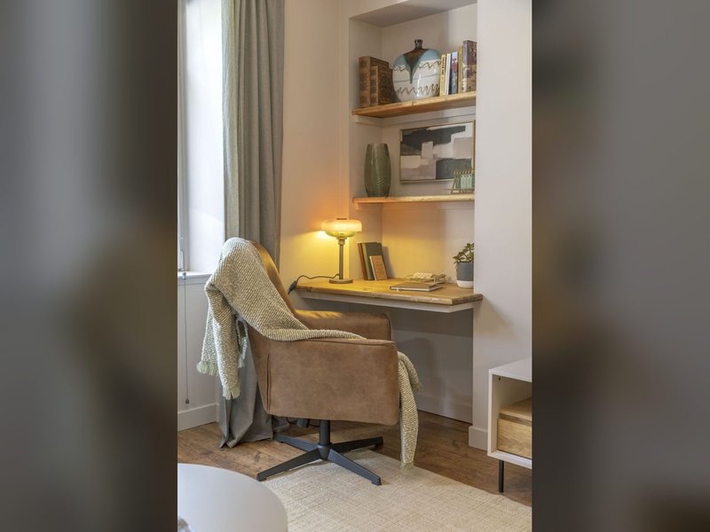 Cozy reading nook with upholstered chair, desk, shelving, lamp and window