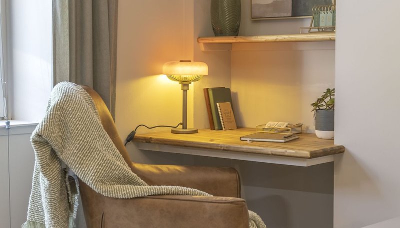 Cozy home office nook with upholstered chair, desk lamp, books and potted plant