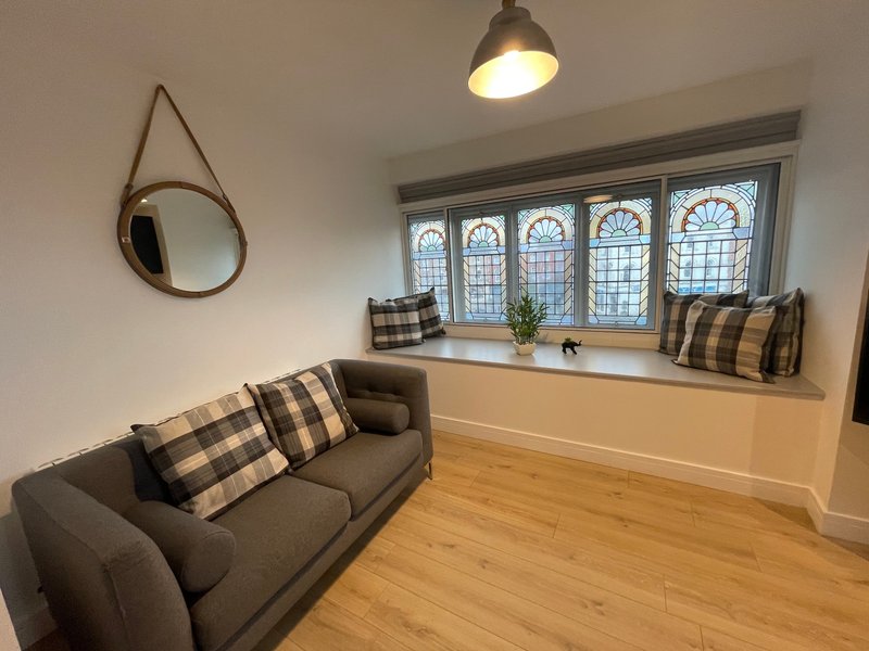Living room with grey sofa, round mirror, pendant lamp, and large window seat with cushions