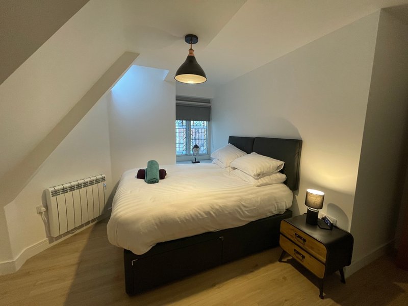 Attic bedroom with black bed, white bedding, pendant lamp, wooden floor and skylight window
