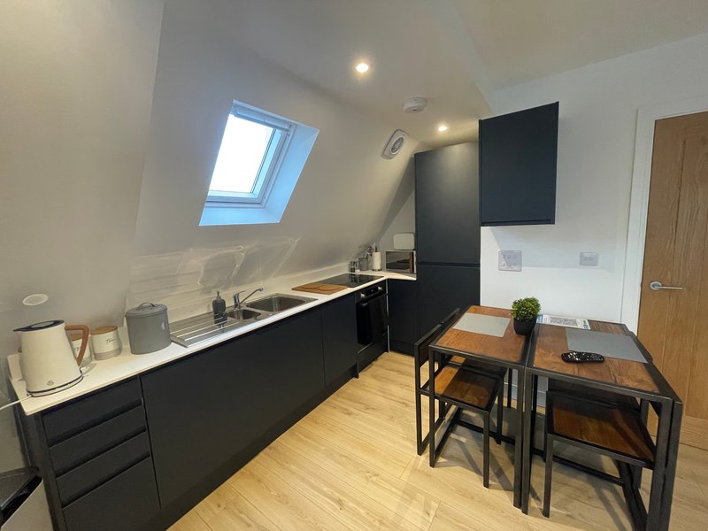 Modern kitchenette with black cabinetry, wooden dining table, skylight window and wooden flooring
