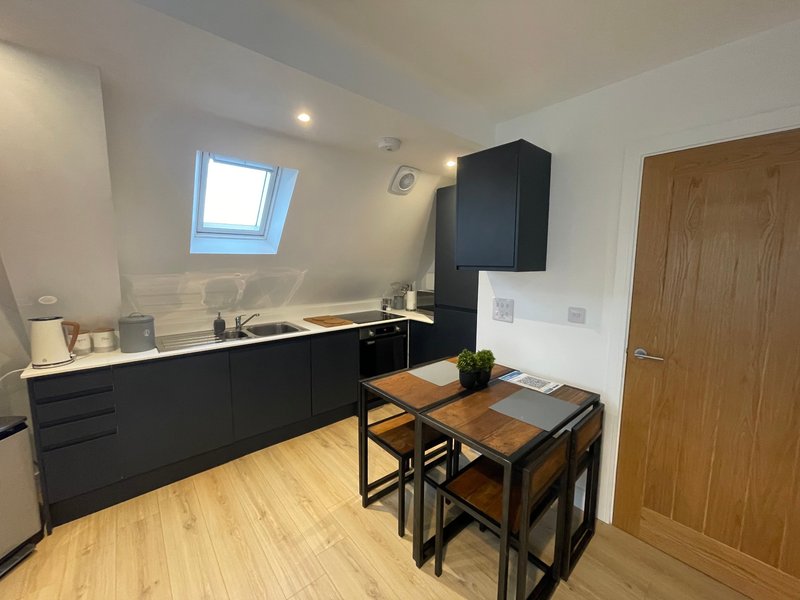 Modern kitchen with black cabinetry, wooden dining table, skylight window and wooden door