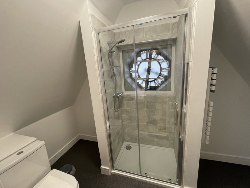 Bathroom with shower cubicle, toilet, and decorative clock window panel