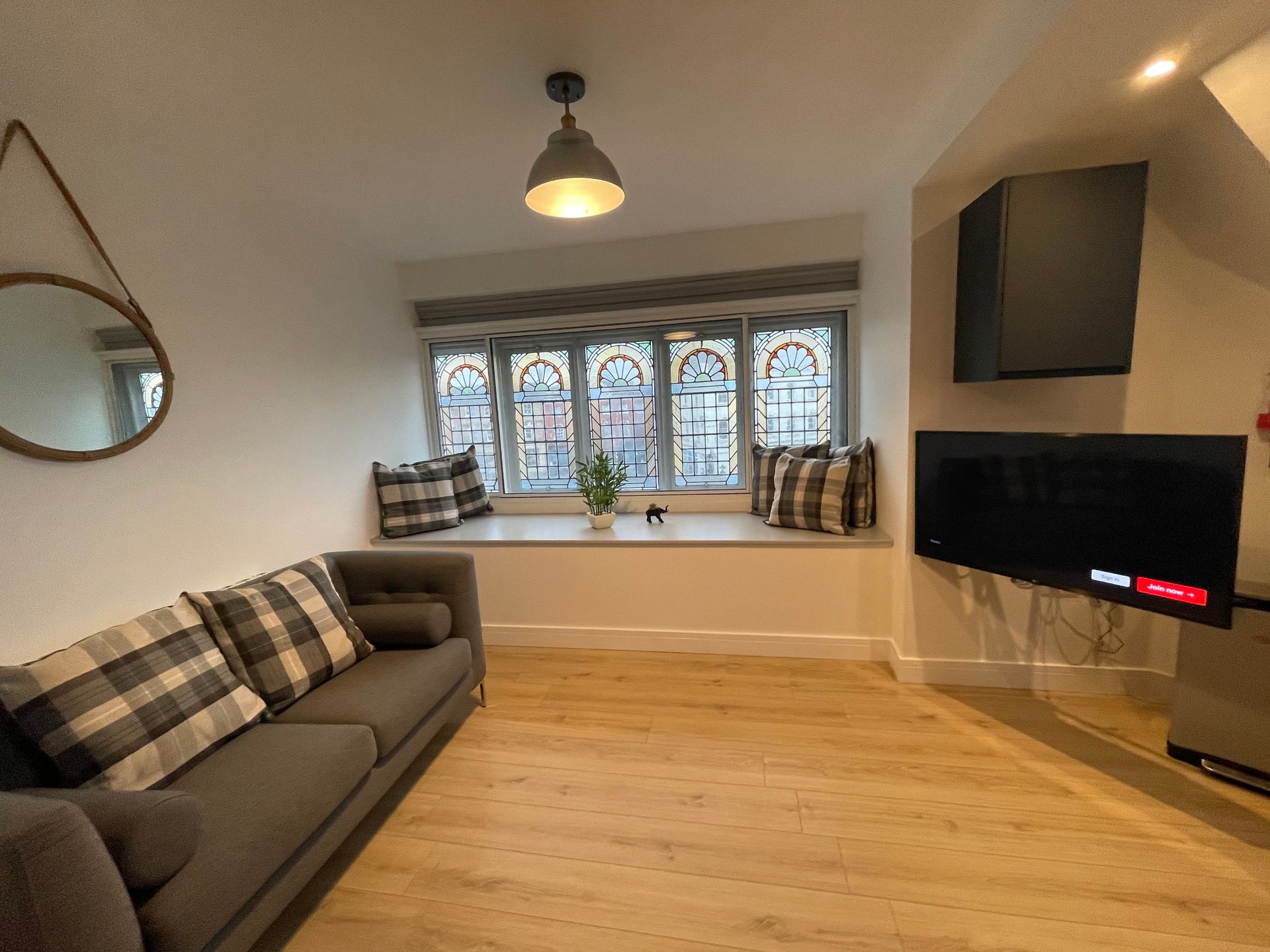 Modern living room with grey sofa, wall-mounted TV, wooden flooring and leaded windows