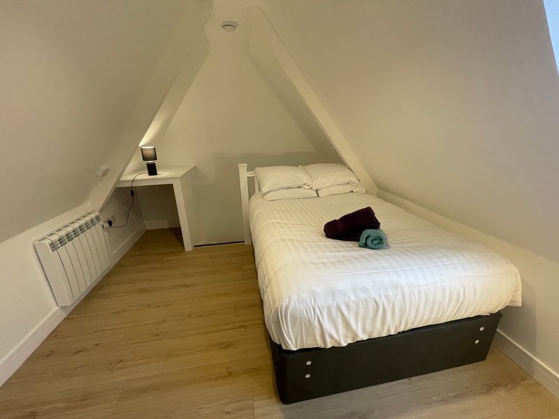 Attic bedroom with sloped ceiling, single bed, wooden floor and bedside table