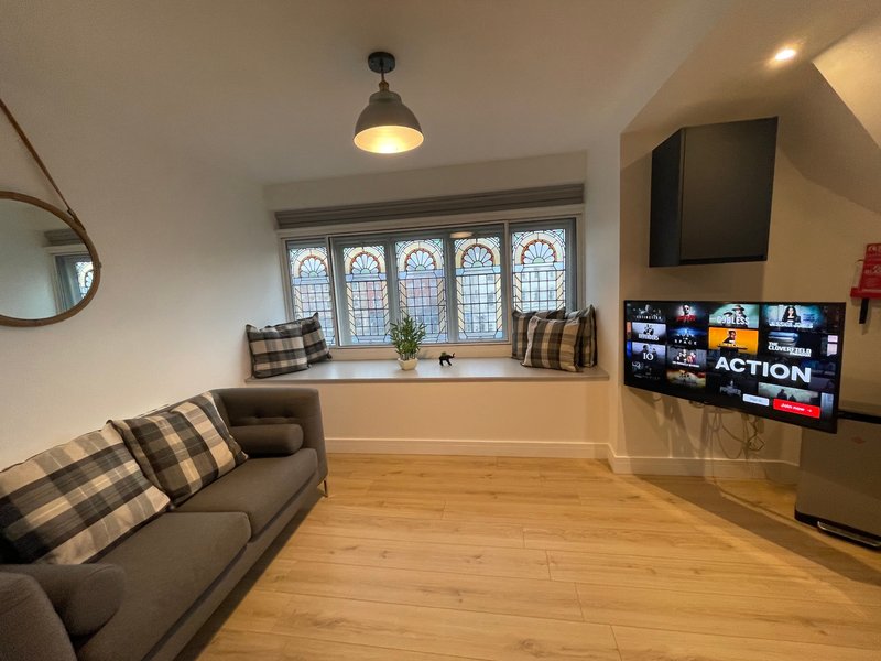 Modern living room with grey sofa, wooden flooring, large window with patterned panes, wall-mounted TV and pendant lighting