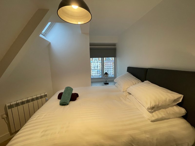 Bright bedroom with double bed, black headboard, pendant lamp and radiator
