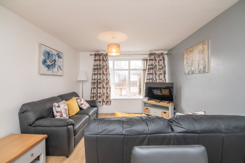 Living room with black leather sofa, TV, window with patterned curtains and wooden floor
