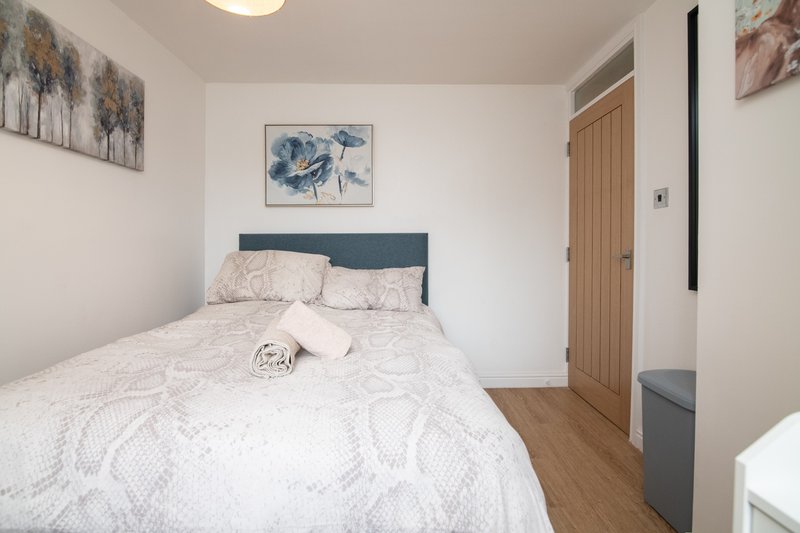 Bright bedroom with double bed, dark headboard, framed artwork, wooden flooring and wardrobe