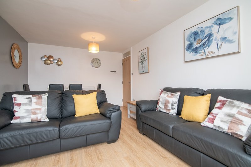 Living room with two black leather sofas, decorative cushions, wooden floor and wall art