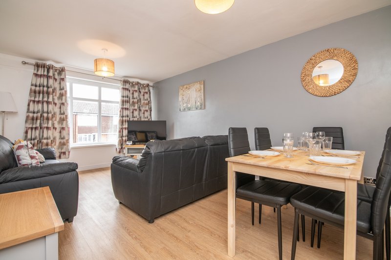 Modern open-plan living and dining area with black leather sofa, wooden dining table, and large window