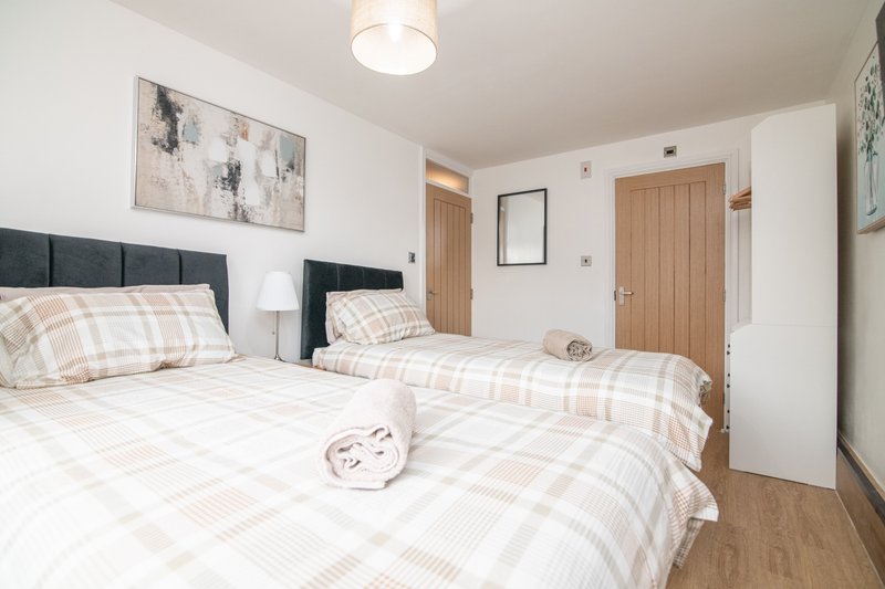 Bright bedroom with two single beds, dark headboards, plaid bedding, wooden doors and flooring