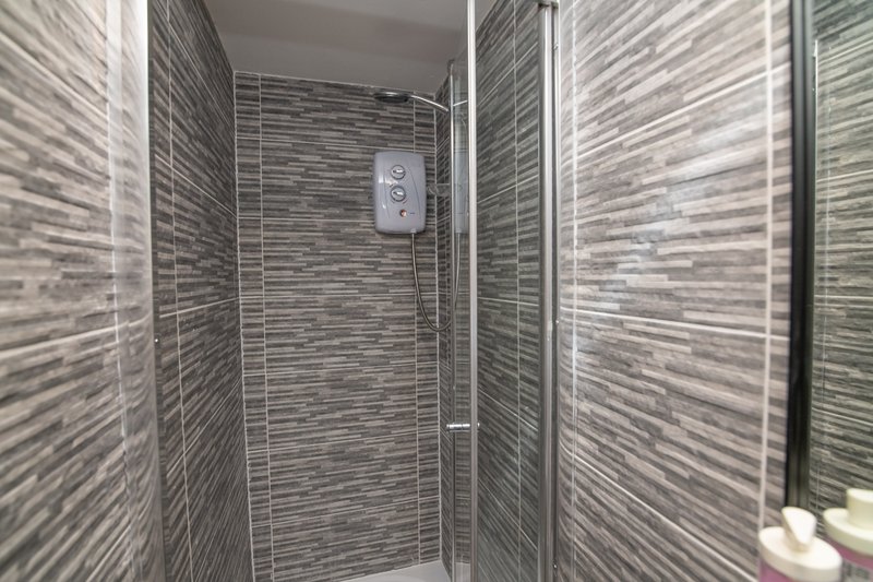 Modern bathroom shower enclosure with grey striped tile walls and glass partition