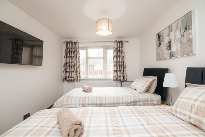 Twin bedroom with plaid bedding, wall-mounted TV, patterned curtains and artwork