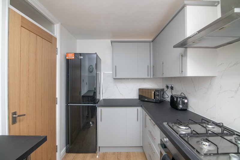 Modern kitchen with white cabinets, black countertop, gas hob, and stainless steel extractor hood