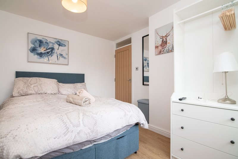 Bedroom with blue-headboard bed, white dresser, framed artwork, and wooden flooring