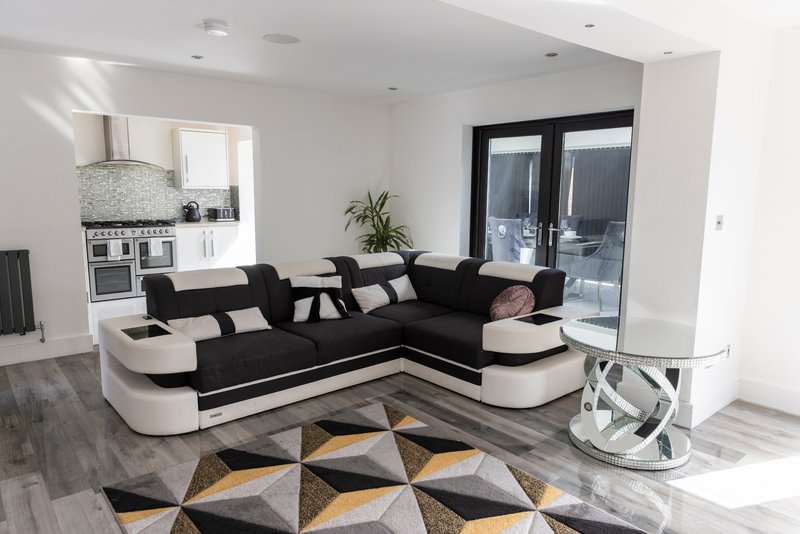 Modern open-plan living room with black and white corner sofa, geometric rug, and kitchen area