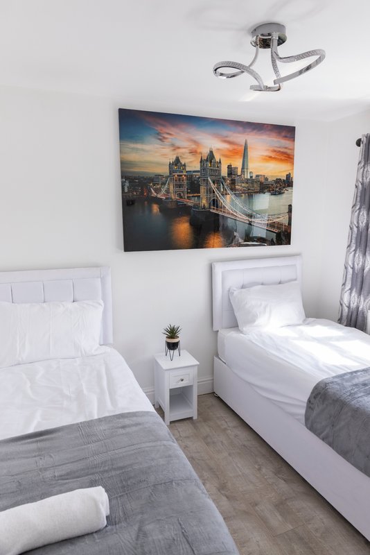 Twin bedroom with white headboards, grey bedding, cityscape wall art and ceiling light