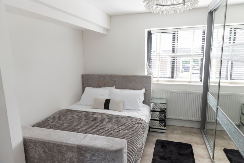Modern bedroom with grey upholstered bed, white bedding, large windows and mirrored wardrobe