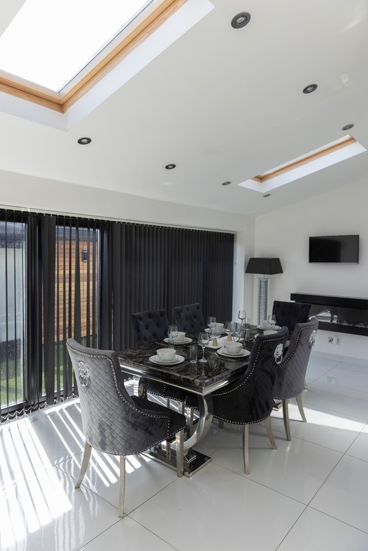 Modern open-plan dining and kitchen area with black table, chairs, skylights and patio doors