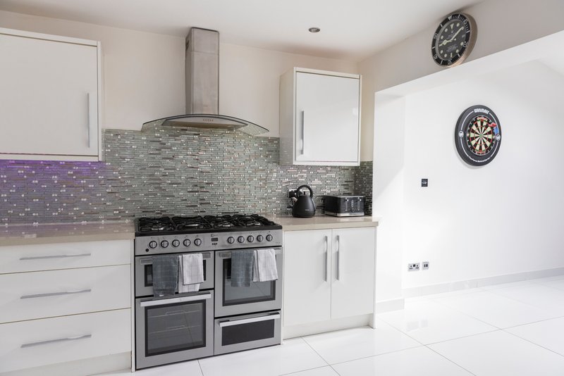 Modern kitchen with white cabinetry, stainless steel range cooker, tiled backsplash and wall clocks