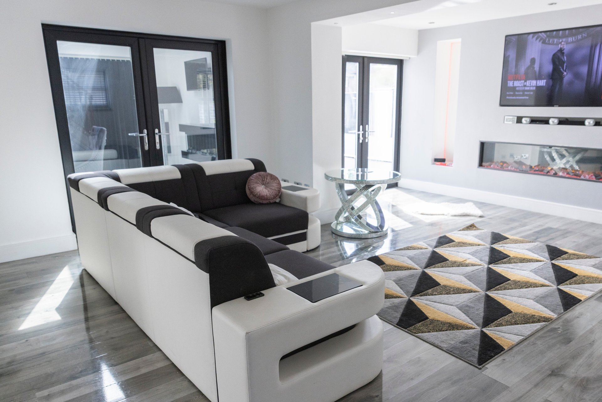 Modern living room with white sofa, black and white striped cushions, geometric floor rug, and wall-mounted TV