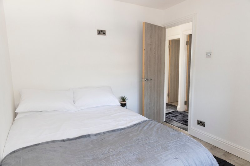 Bright bedroom with double bed, white pillows, grey throw, and open door to ensuite bathroom