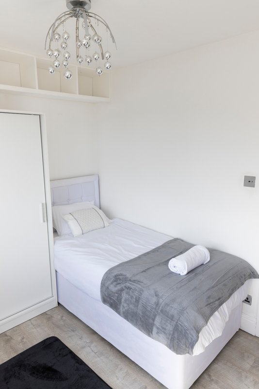 Single bedroom with white bed, grey throw blanket, modern ceiling light fixture
