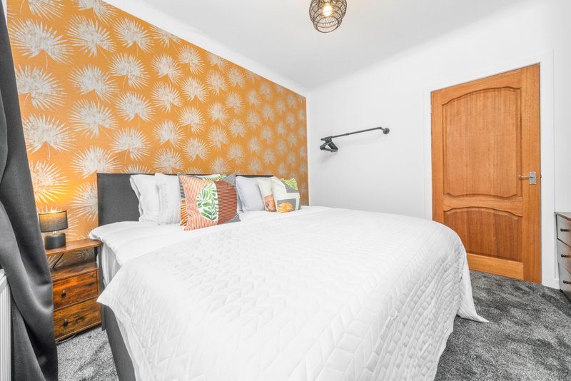 Bedroom with double bed, orange patterned accent wall, wooden door and nightstand