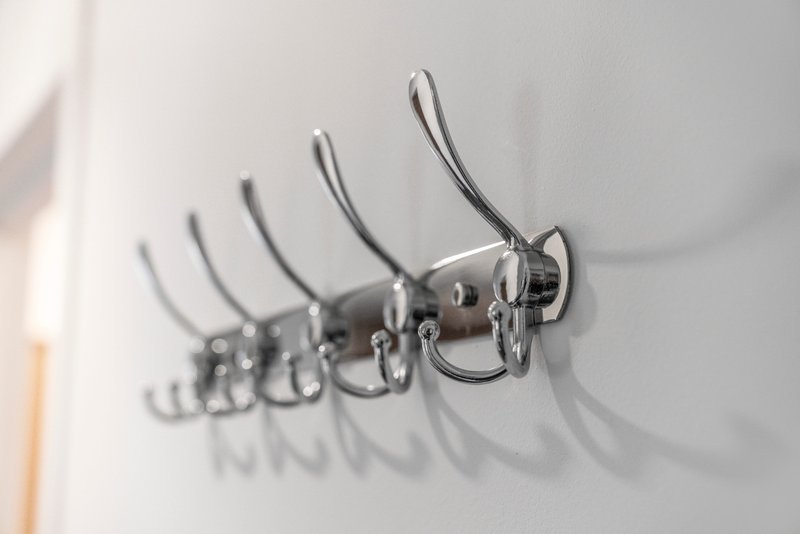 Wall-mounted metal coat hooks with curved arms on white wall