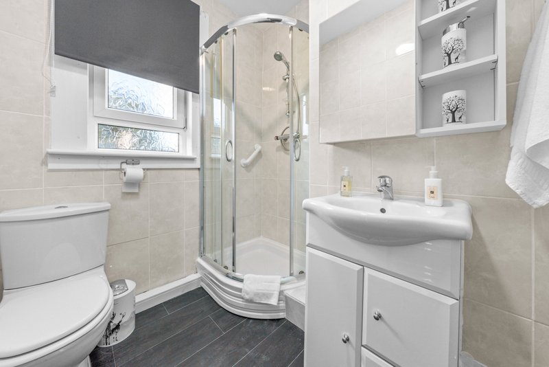 Modern bathroom with shower enclosure, toilet, white vanity sink and shelving