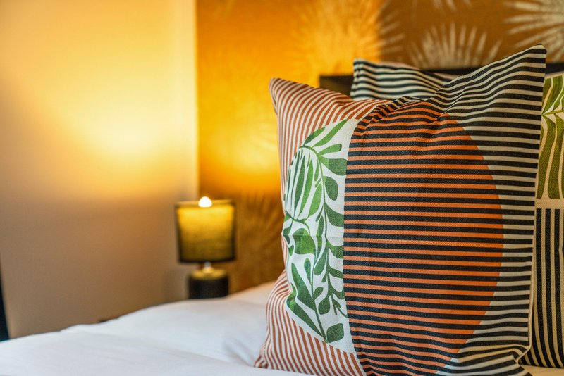 Bedroom with white bedding, striped decorative pillows, warm ambient lighting, and candle on nightstand