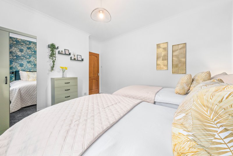 Bright bedroom with two single beds, yellow patterned cushions, wooden door, and wall art