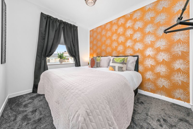 Bedroom with double bed, orange patterned accent wall, grey carpet and window with dark curtains