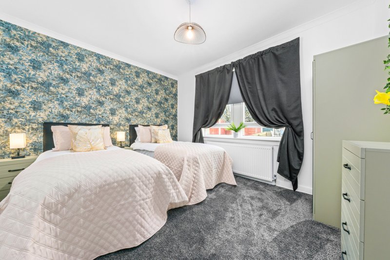Bedroom with two single beds, patterned feature wall, dark curtains and green dresser
