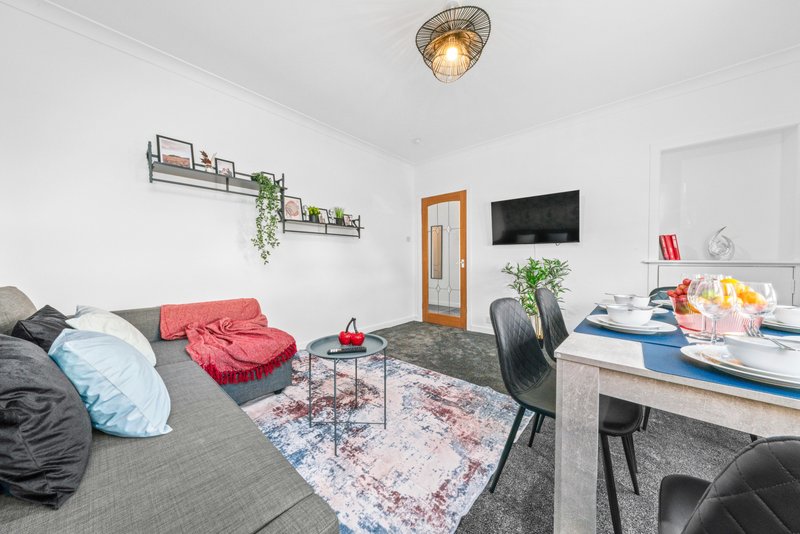 Open-plan living and dining area with sofa, cushions, dining table, wall-mounted shelves and ceiling light