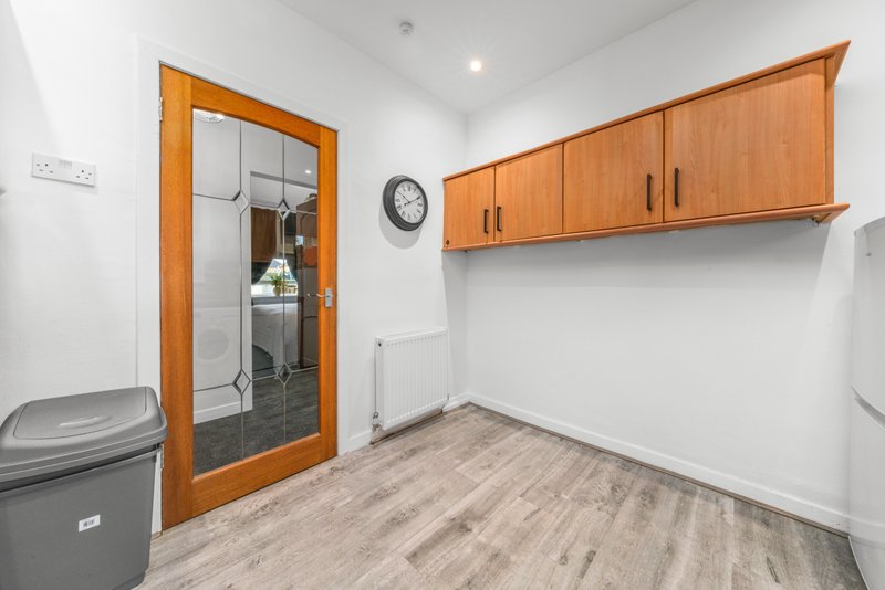 Utility room with wooden cabinets, wall clock, grey bin and laminate flooring