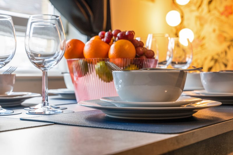 Dining table set with white plates, glasses, and bowl of fresh oranges and grapes
