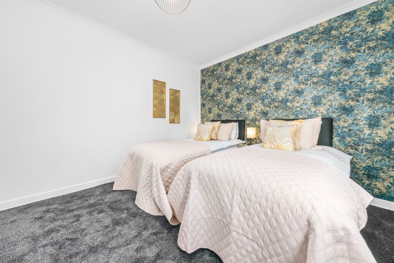 Bedroom with two single beds, patterned teal headboard, white bedding, and gold wall art