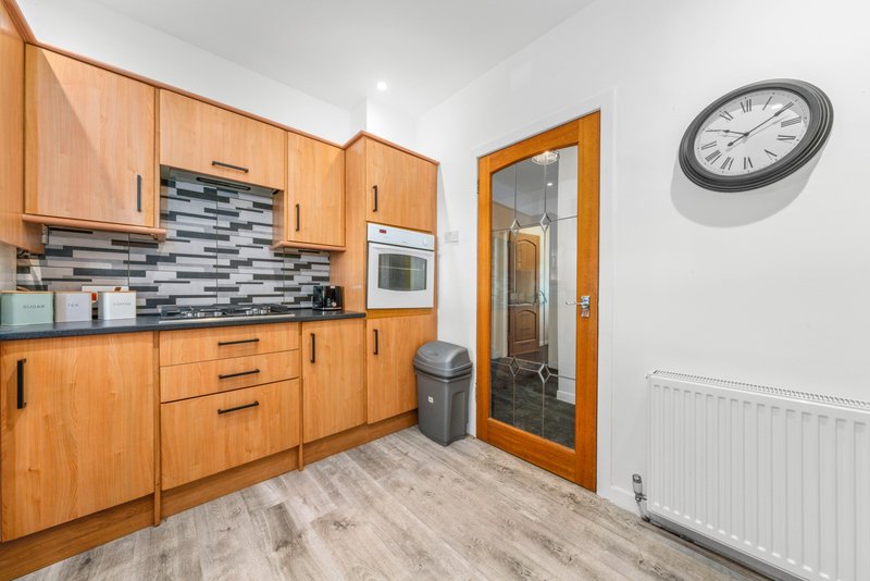 Modern kitchen with wooden cabinets, tiled backsplash, white appliances and wall clock