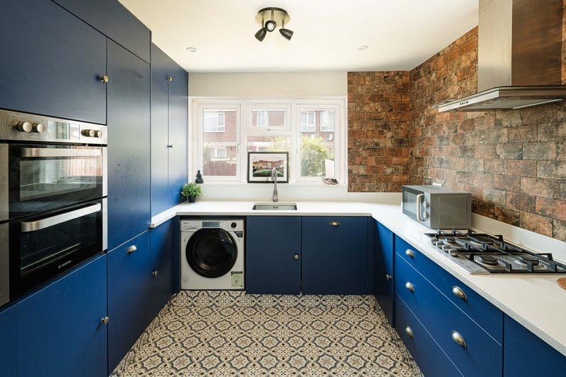 Modern kitchen with blue cabinetry, brick splashback, integrated washing machine and gas hob