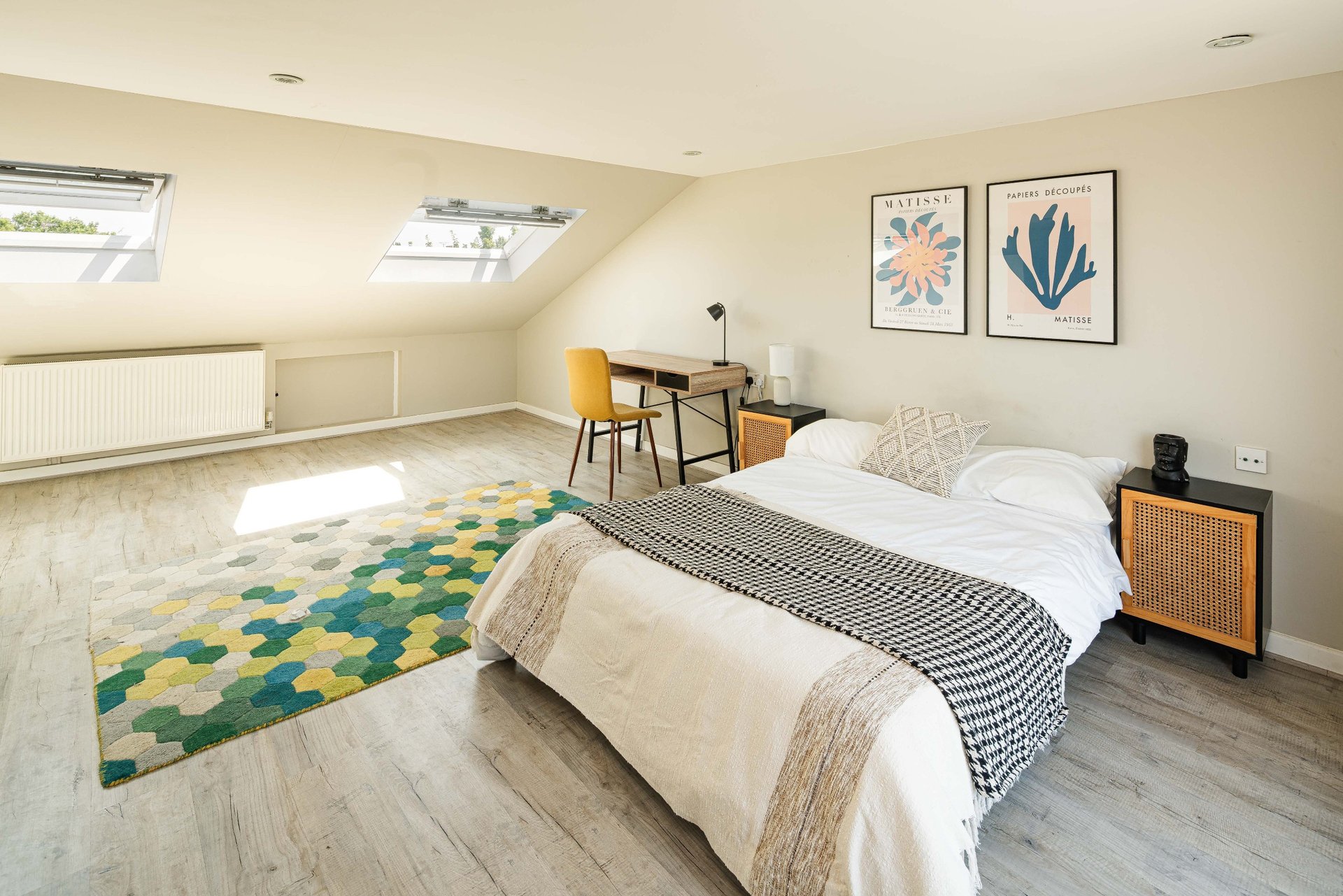 Bright attic bedroom with double bed, desk area, colorful rug and framed wall art