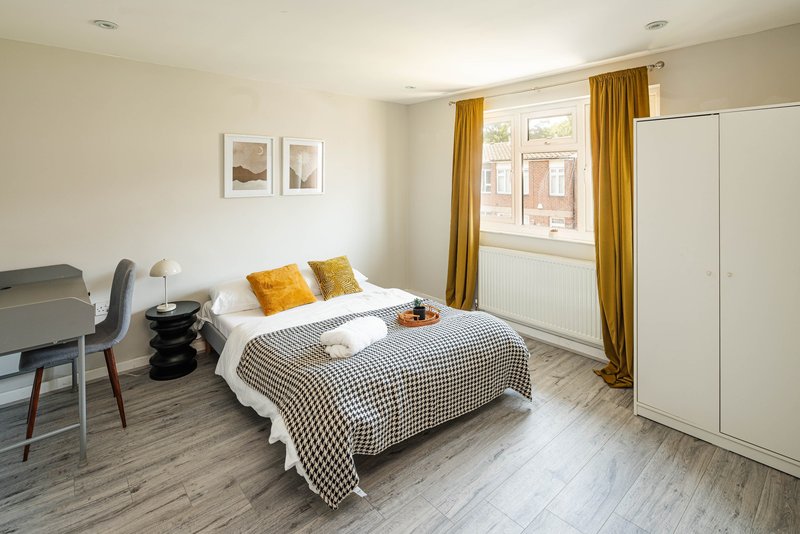 Bright bedroom with double bed, yellow curtains, desk chair and white wardrobe