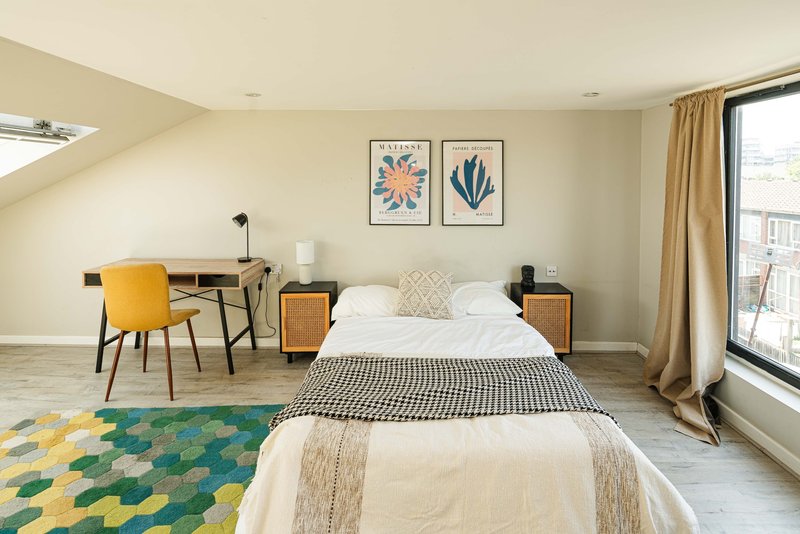 Bright attic bedroom with double bed, desk, yellow chair and sloped ceiling