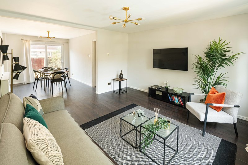 Open-plan living room with cream sofa, TV wall, dining area, and potted plants