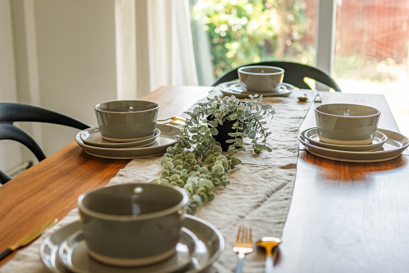 Dining table set for four with place settings, centerpiece plant, and garden view