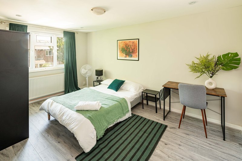 Bright bedroom with single bed, green bedding, desk area, framed artwork, and window with green curtains
