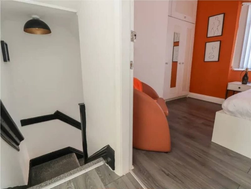 Modern bedroom with orange accent wall, wooden flooring, pendant light and contemporary furniture