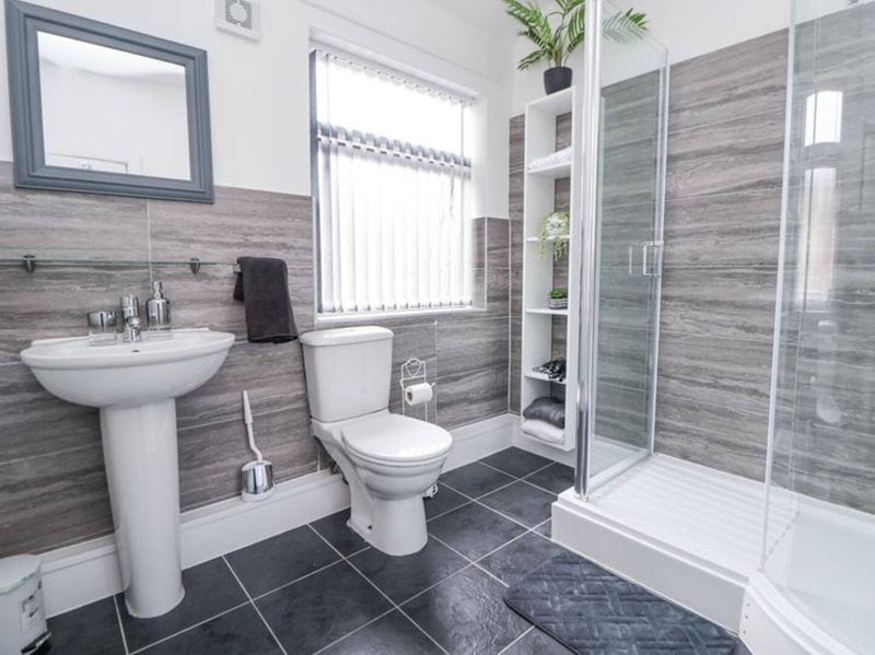 Modern bathroom with pedestal sink, toilet, shower enclosure and wood-grain tile walls